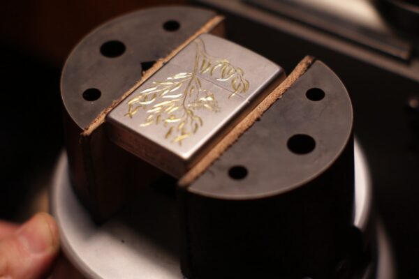 Hand-engraved bright-cut gum leaves on a nickel-plated Zippo, revealing a striking two-tone contrast.